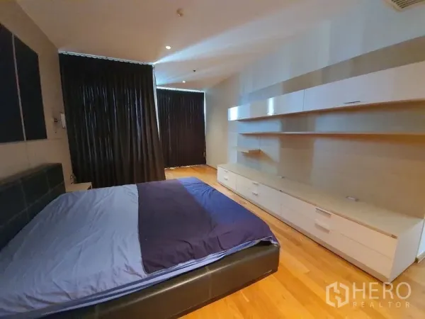 คอนโด ขาย - ห้องนอนหลักพื้นไม้ ผ้าม่านทึบ และตู้บิลท์อินยาวตามผนัง