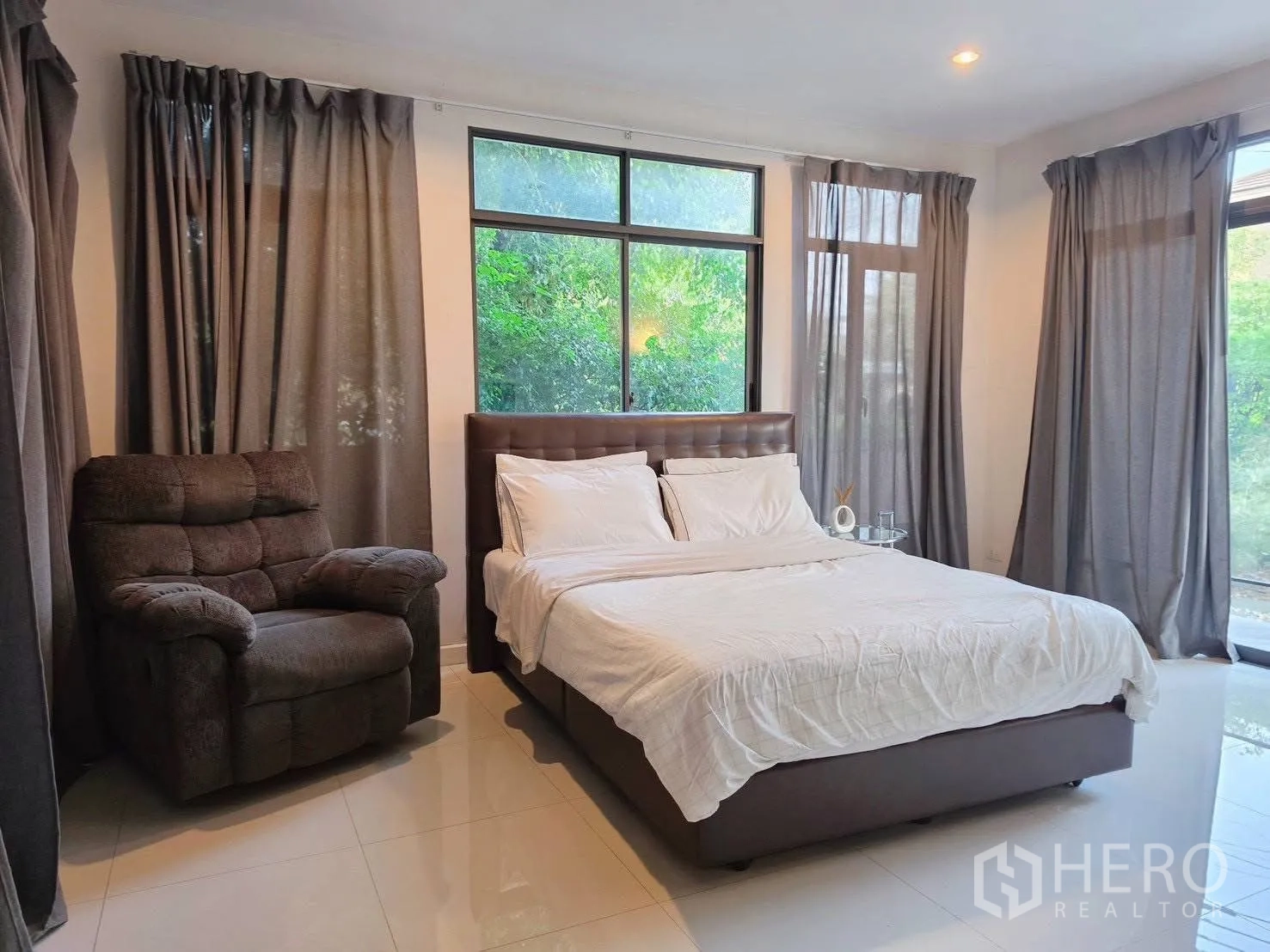 Detached House for rent or sale in Suan Luang, Bangkok - Corner bedroom with large windows, bed and recliner chair.