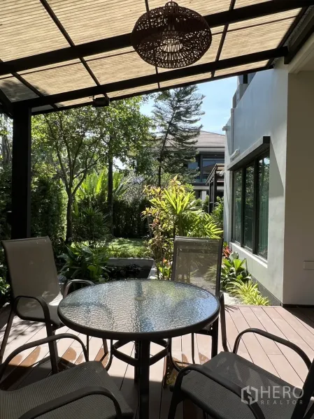บ้าน ให้เช่าในBang Kapi, Bangkok - เฉลียงมีหลังคาพร้อมโต๊ะกระจกและเก้าอี้ มองสู่สวนเขียวชอุ่ม