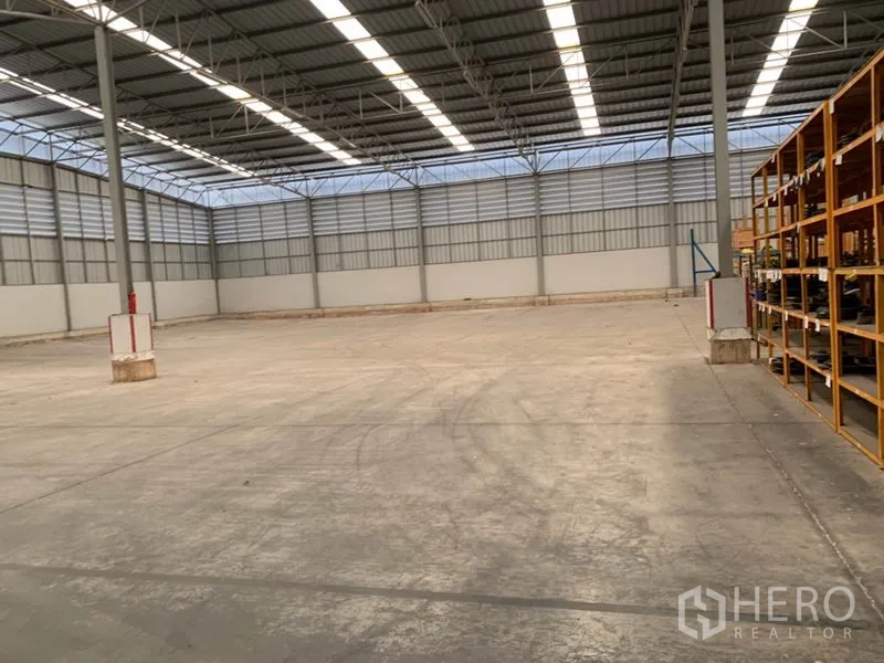 货栈 出租在Khlong Sam Wa, Bangkok - 仓库内景：混凝土地面、天窗、支撑柱，右侧为货架区。