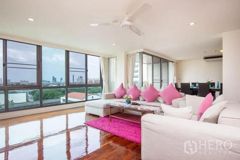 Condominium for rent in Bang Rak, Bangkok - Corner living area with pink accents, ceiling fan and wraparound windows showing wide city views.