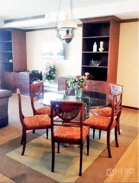 Condominium for rent or sale in Watthana, Bangkok - Glass-top dining table for four under a pendant light, flanked by built-in bookshelves.