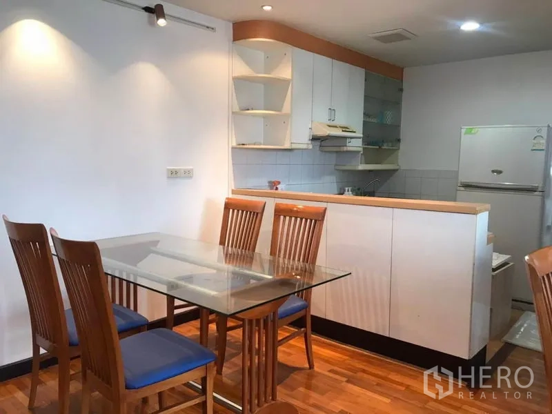 公寓 出租或出售在Khlong Toei, Bangkok - 玻璃餐桌与木椅，旁边是白色橱柜的小厨房和冰箱
