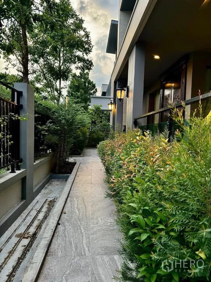 Detached House for sale in Saphan Sung, Bangkok - Landscaped side walkway lined with trimmed hedges and classic wall lanterns beside the house.