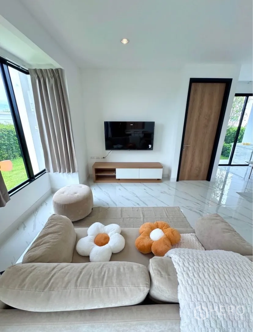 Detached House for rent in Samut Prakan - Bright living room with TV wall, beige sofa and marble-look tiled floor.