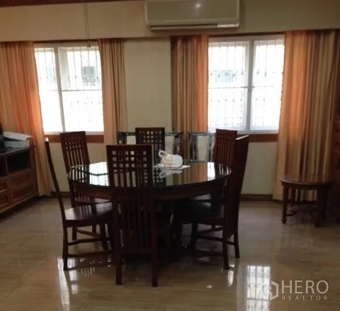 Detached House for rent in Bang Rak, Bangkok - Formal dining area with round glass-top table, six wooden chairs and twin windows with curtains.