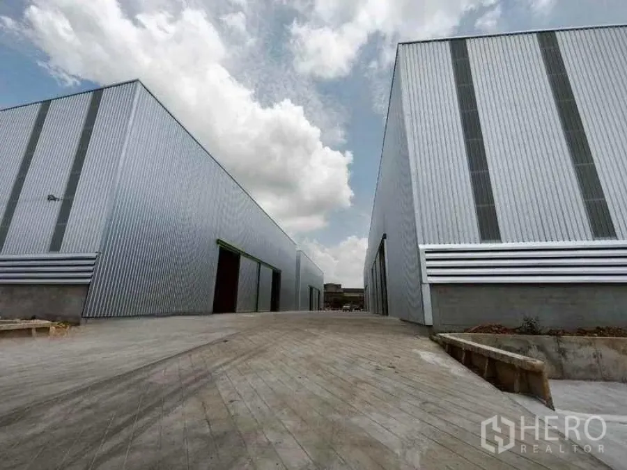 货栈 出租在Bang Phli, Samut Prakan - 邦普里金属板仓库外观，宽阔的混凝土车道与晴朗天空。