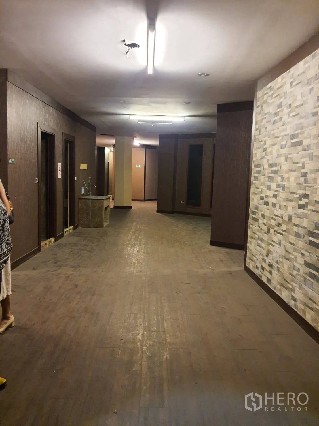 Shophouse for rent in Khlong Toei, Bangkok - Spacious floor with wood-look flooring, stone accent wall, multiple doorways and fluorescent ceiling lights.