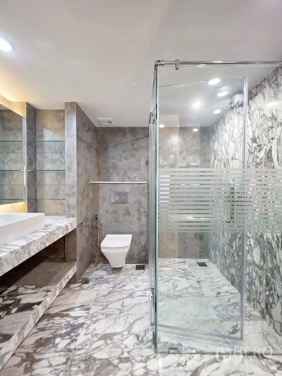 Condominium for rent in Sathon, Bangkok - Marble-clad bathroom with glass walk-in shower and wall-hung toilet.