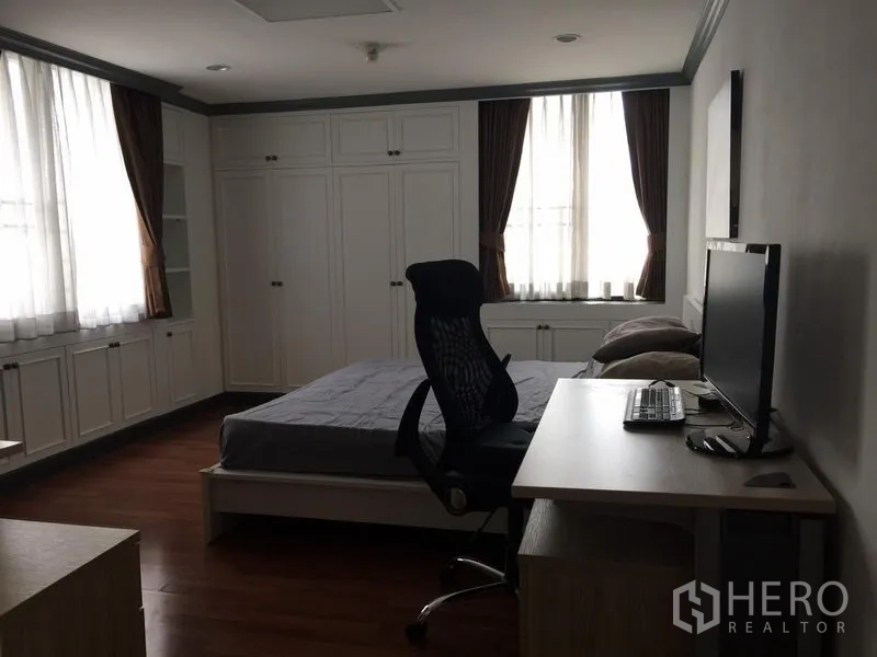Condominium for rent in Watthana, Bangkok - Spacious bedroom with desk and computer setup, built-in wardrobes and two curtained windows.
