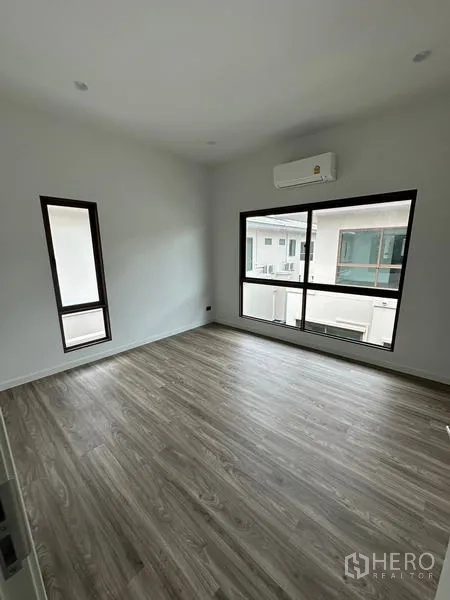 Detached House for rent in Bang Kapi, Bangkok - Spacious bedroom with large window and wall AC overlooking the neighborhood.