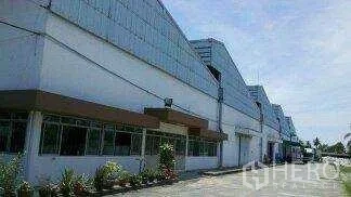 Warehouse for rent in Khlong Toei, Bangkok - Side view of connected warehouse buildings with windows and a driveway under a clear sky.