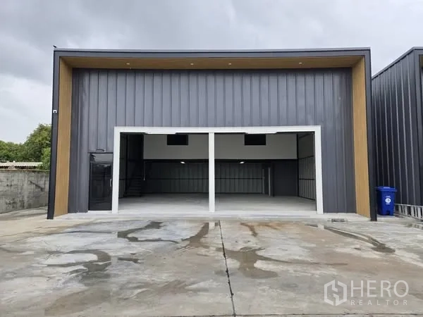 Warehouse for rent - Front elevation of modern dark-panel warehouse with twin wide openings and a concrete forecourt.