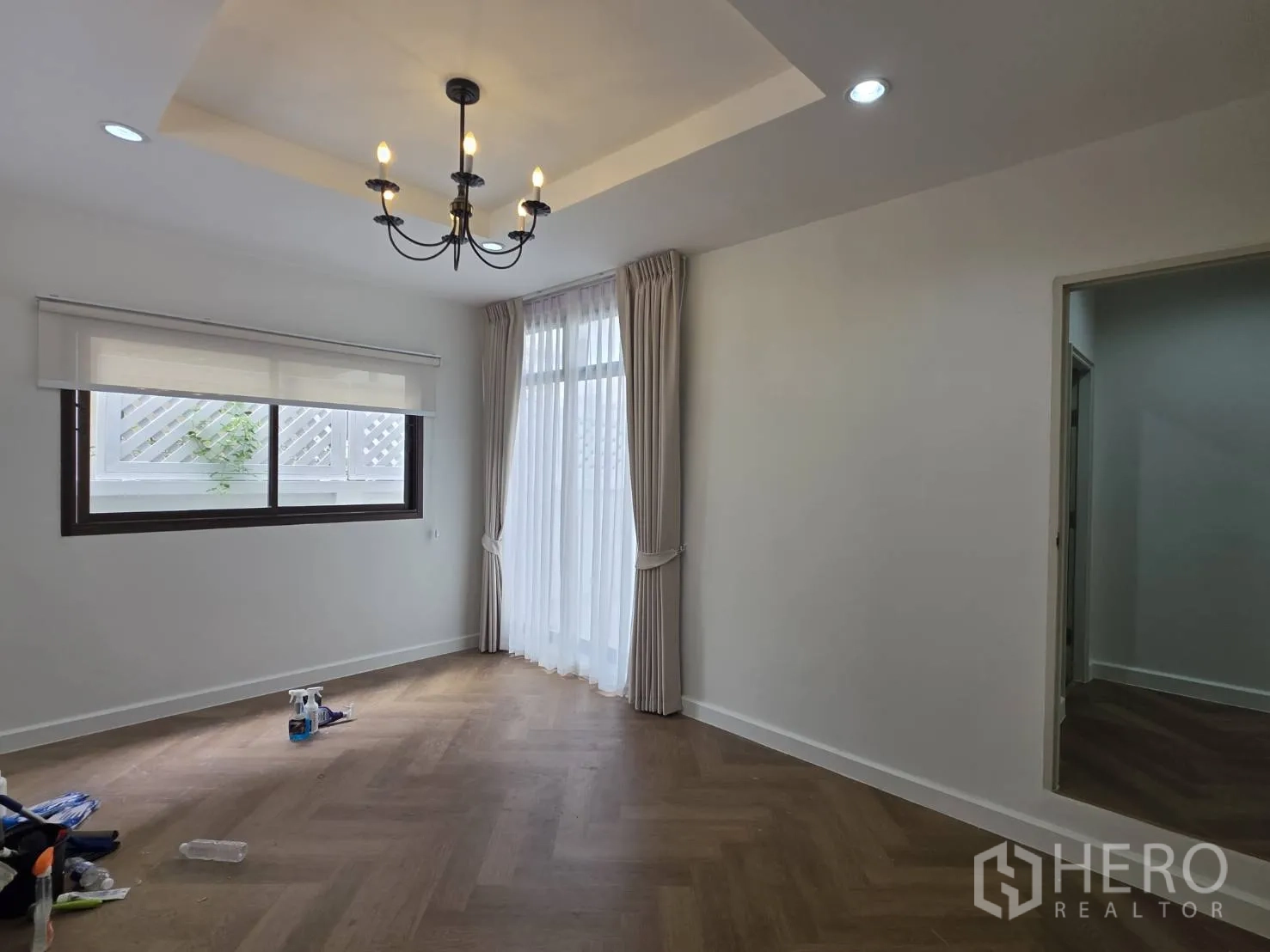 Detached House for sale in Lam Luk Ka, Pathum Thani - Bright room with tray ceiling, chandelier, wood-look flooring, and large windows with curtains.