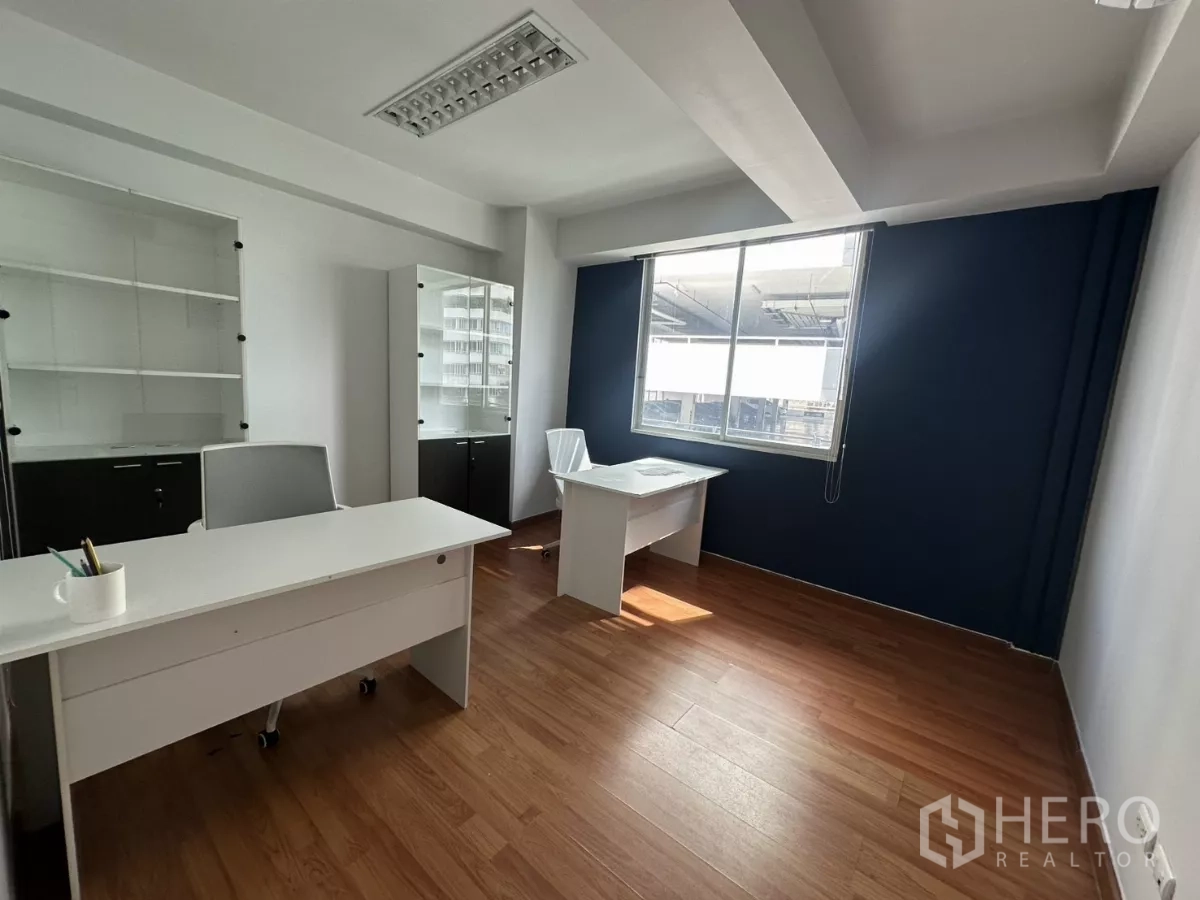 Office Space for rent in Watthana, Bangkok - Private office with two white desks, large window and display cabinets against a dark blue feature wall.