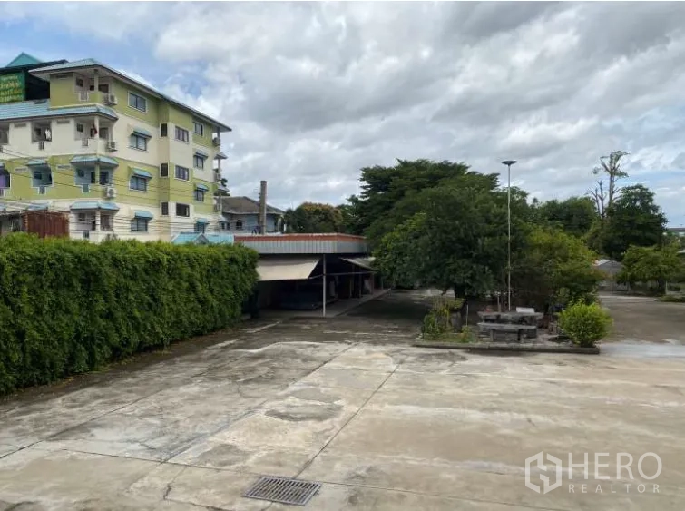Land for sale in Lat Krabang, Bangkok - Wide concrete courtyard with greenery, a covered structure, and perimeter hedge.
