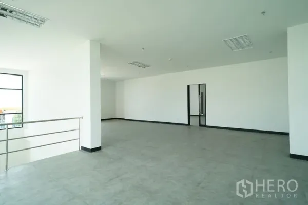 Warehouse for rent in Khlong Luang, Pathum Thani - Open-plan mezzanine office area with railing, white walls, and gray floor tiles.