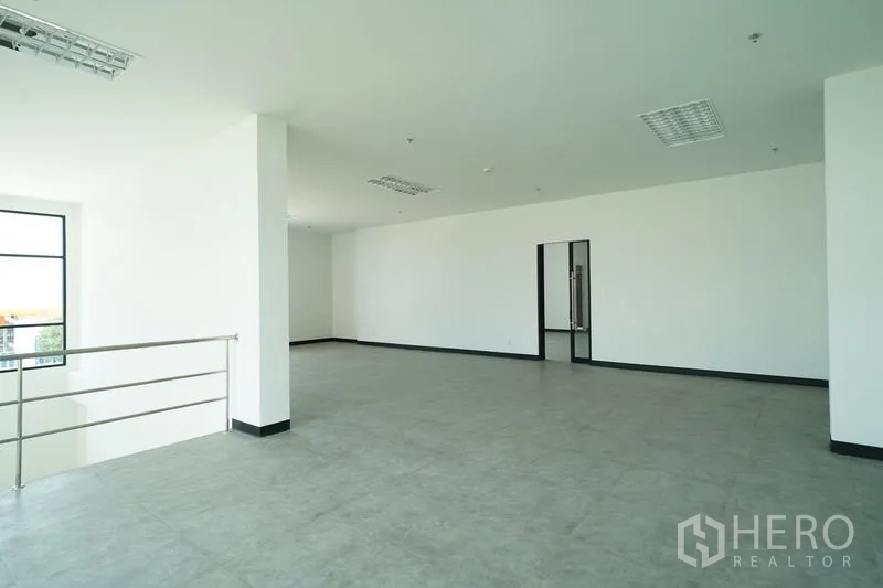 Warehouse for rent in Khlong Luang, Pathum Thani - Open-plan mezzanine office area with railing, white walls, and gray floor tiles.