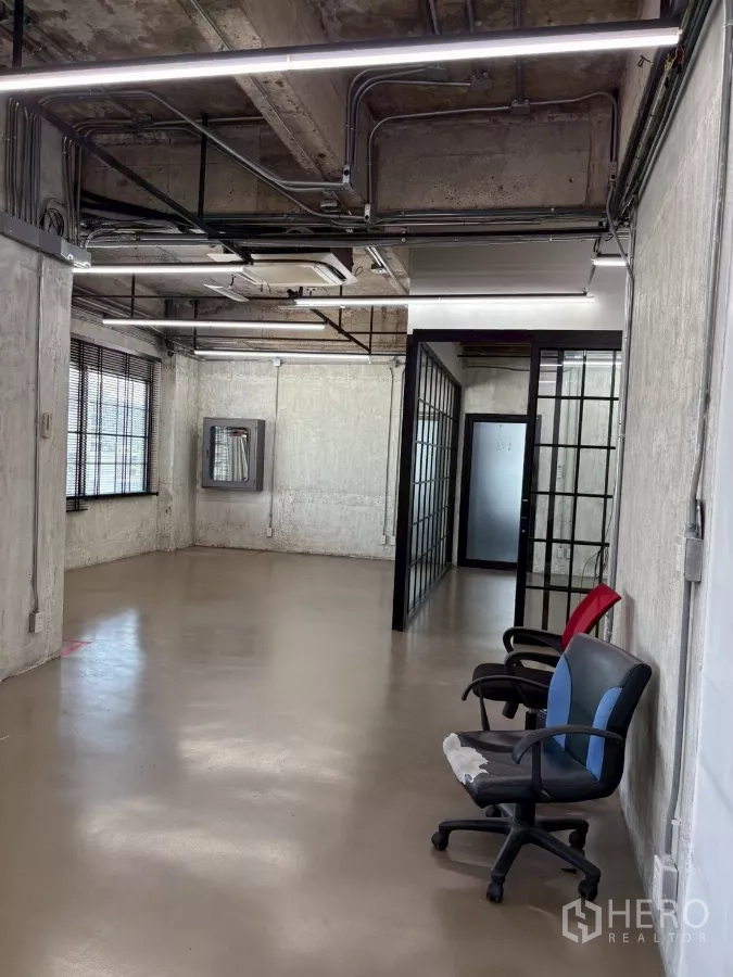 Office Space for rent in Watthana, Bangkok - View to the entrance with frosted door, grid glass walls and industrial ceiling conduits.