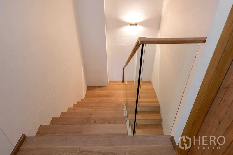 Condominium for rent in Phra Khanong, Bangkok - Wood staircase with glass balustrade and soft wall light in a modern condominium.