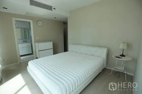 Condominium for rent or sale in Watthana, Bangkok - Bright master bedroom with white upholstered bed, side table, and access to an ensuite bathroom.