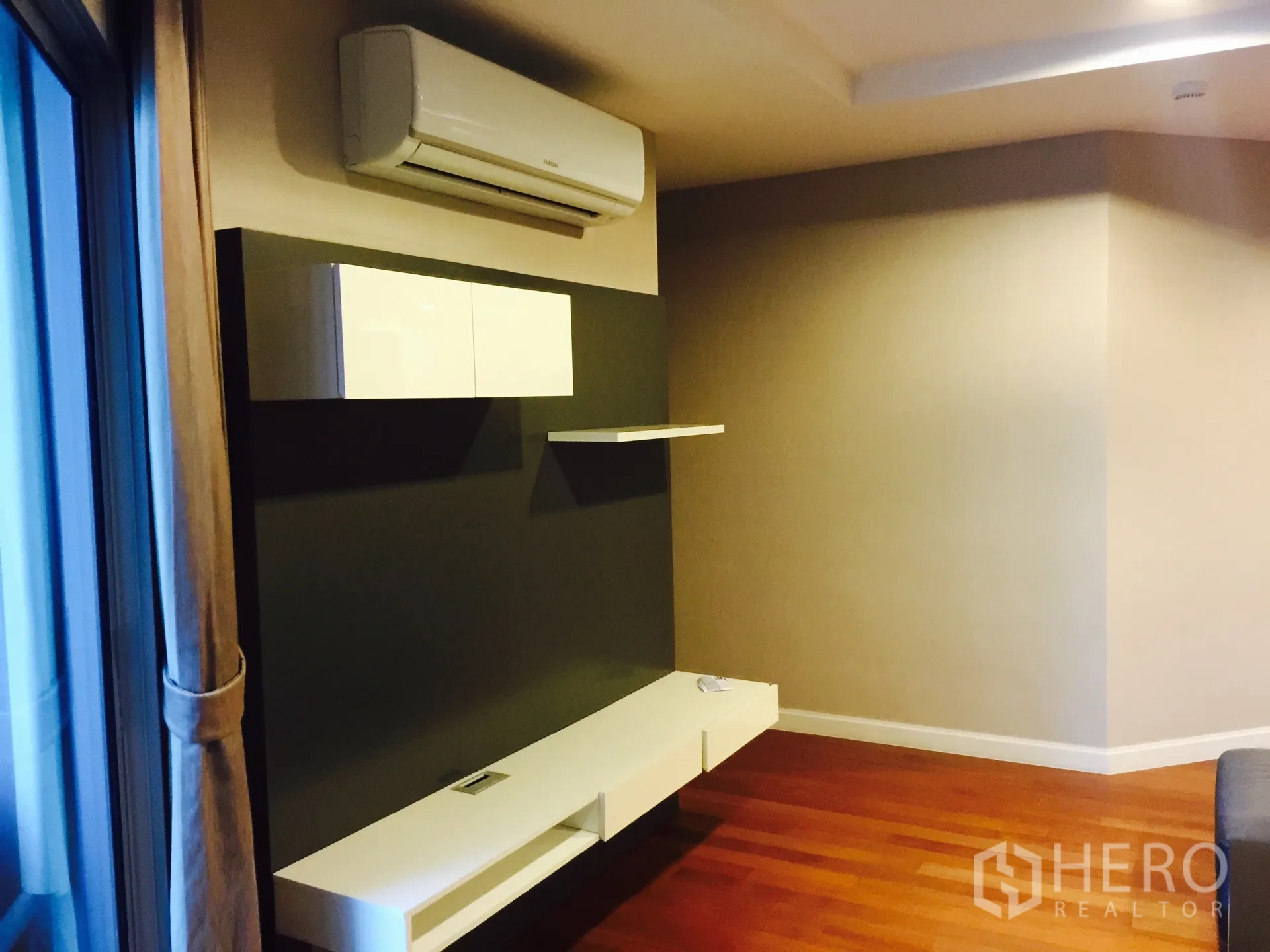 Condominium for rent in Huai Khwang, Bangkok - Minimalist media wall with floating shelves and split air conditioner beside a large window.
