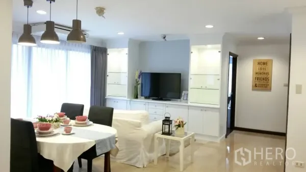 Condominium for rent or sale in Watthana, Bangkok - Bright open-plan living and dining area with TV cabinet and round table beside full-height windows.