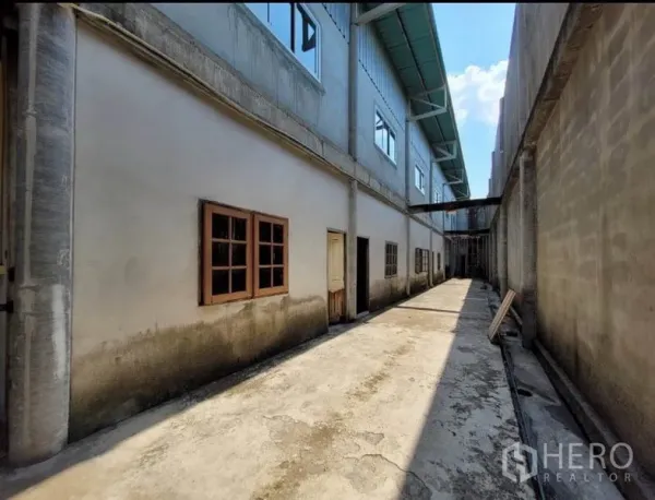 Warehouse for rent or sale in Sai Noi, Nonthaburi - Narrow service alley between warehouse blocks with windows and multiple access doors.