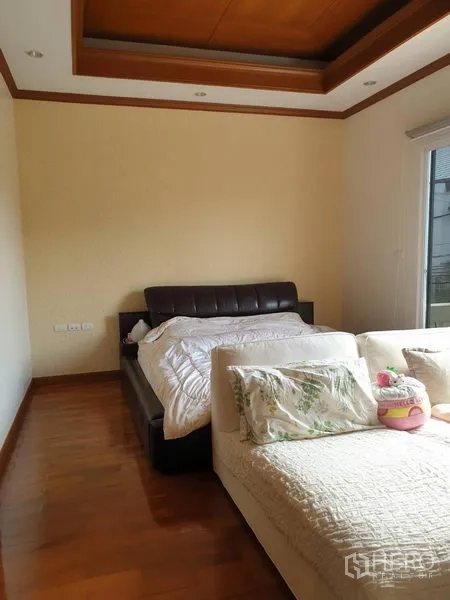 Townhouse for rent in Bang Kho Laem, Bangkok - Spacious bedroom with leather bed and sofa, wood flooring and tray ceiling.
