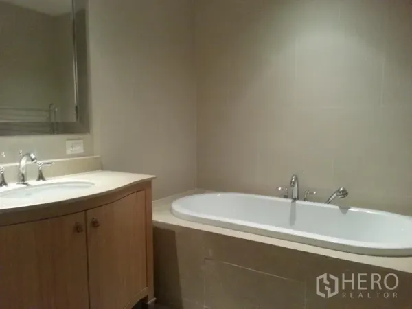 Condominium for rent in Sathon, Bangkok - Modern bathroom with a built-in bathtub, stone vanity, and neutral tile walls.