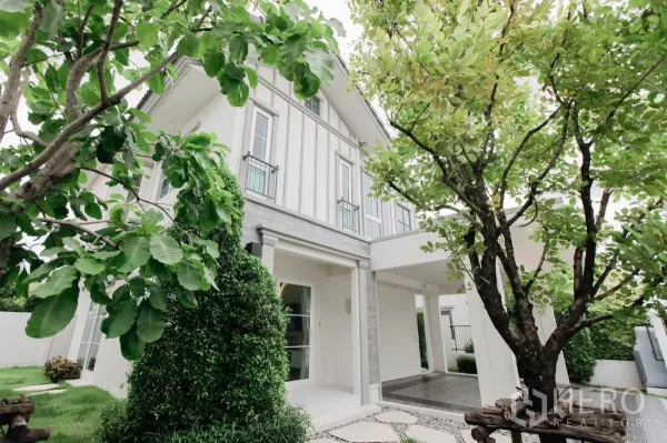 独立式住宅 出租或出售在Bang Phli, Samut Prakan - 房屋侧面，修剪整齐的草坪、大树与通往车棚的小径。