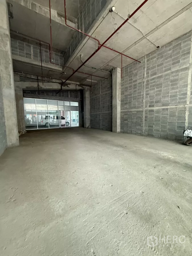 Retail Space for rent in Bang Rak, Bangkok - Unfurnished double-height retail unit with exposed red sprinkler pipes and a wide glass storefront facing the street in Bang Rak.