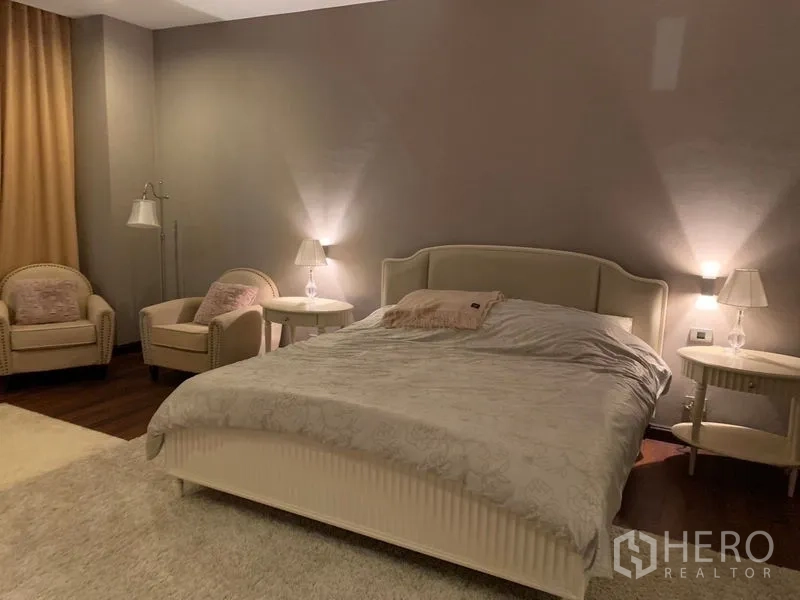 Townhouse for sale in Watthana, Bangkok - Spacious bedroom with king bed, bedside lamps, lounge chairs and heavy curtains.