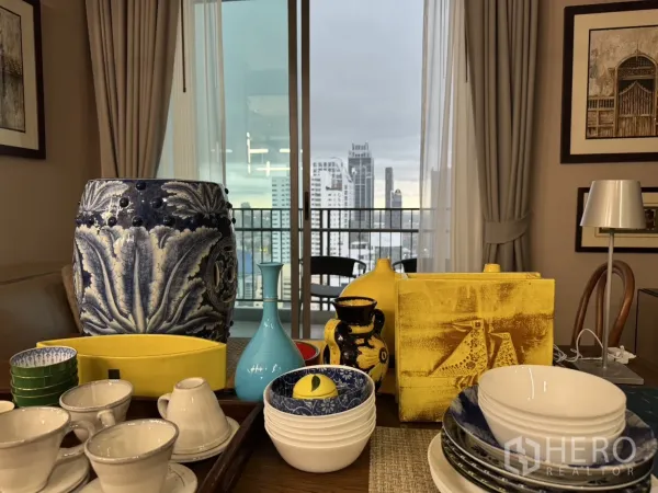 คอนโด ให้เช่าในWatthana, Bangkok - โต๊ะอาหารพร้อมเครื่องใช้สีสันสดใส มองออกระเบียงเห็นวิวสกายไลน์ผ่านประตูกระจก