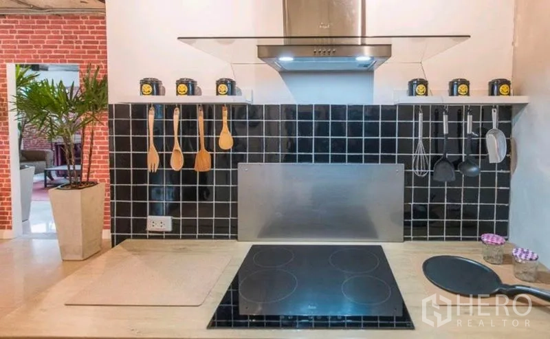 Condominium for rent in Watthana, Bangkok - Modern cooktop and hood with black tile backsplash and hanging utensils.
