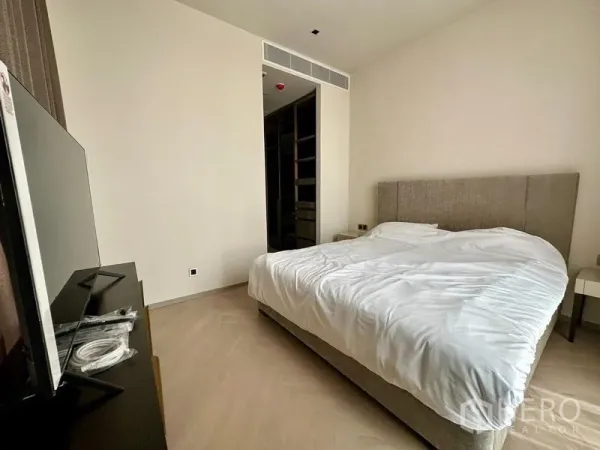 公寓 出租 - 温馨卧室，软包床、白色床品、电视柜，并通往步入式衣帽间。