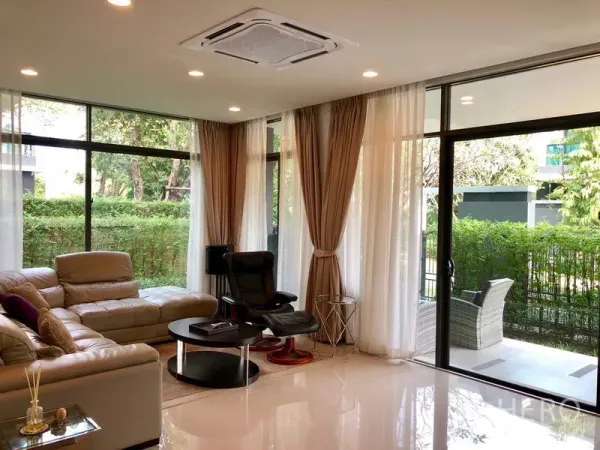 Detached House for rent or sale in Bang Kapi, Bangkok - Bright living room with leather sofa, floor-to-ceiling windows and garden views.