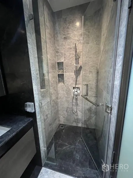 Condominium for rent - Close-up of frameless glass shower with handheld spray and recessed shelves.