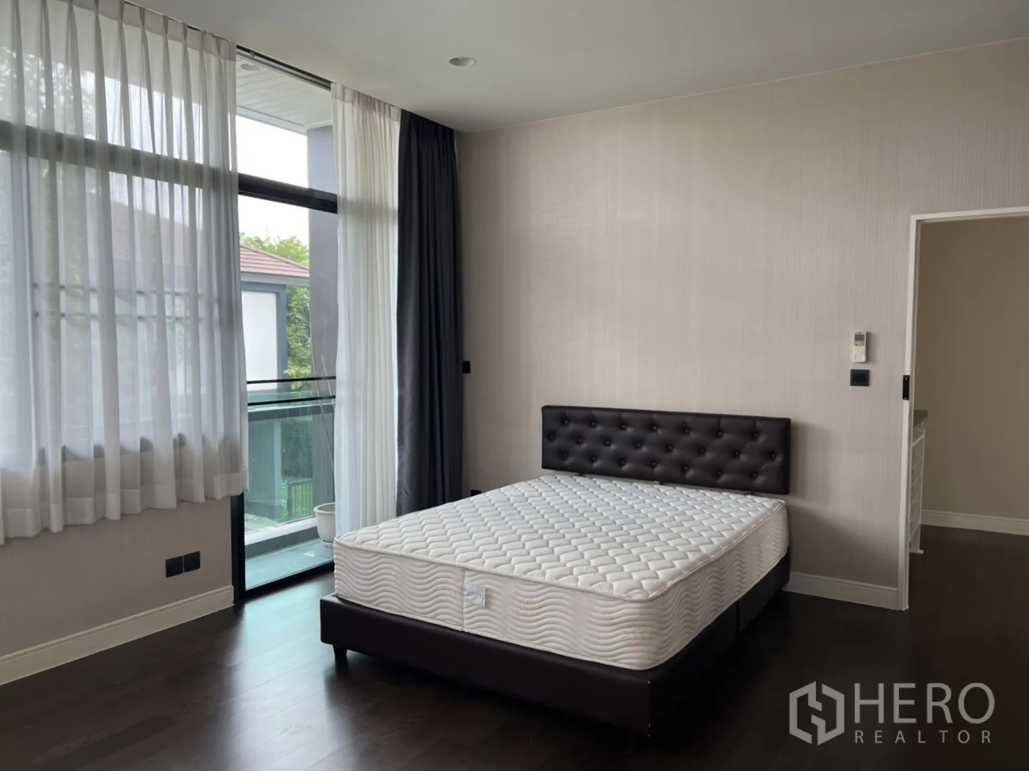 Detached House for rent or sale in Bang Kapi, Bangkok - Master bedroom with corner glazing, balcony access and mattress on dark bed frame.