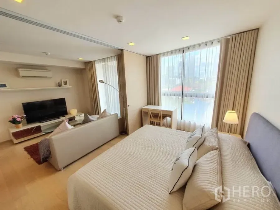 คอนโด ให้เช่าในWatthana, Bangkok - คอนโดแผนผังเปิดสว่าง มีเตียงคิง โซฟา ทีวี และโต๊ะทำงานข้างหน้าต่างบานใหญ่เห็นวิวเมือง