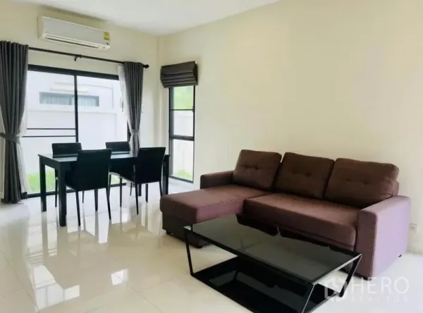 Townhouse for rent in Saphan Sung, Bangkok - Bright living and dining area with L-shaped sofa, glass coffee table, four-seat dining set and large windows.