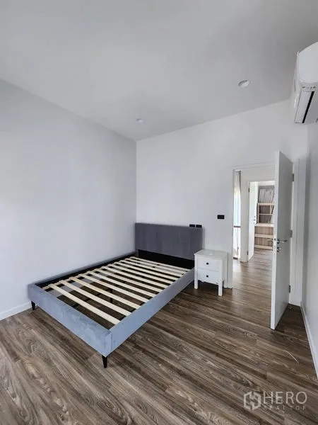 Detached House for rent in Bang Kapi, Bangkok - Minimal bedroom with bed frame, bedside table and wood flooring.