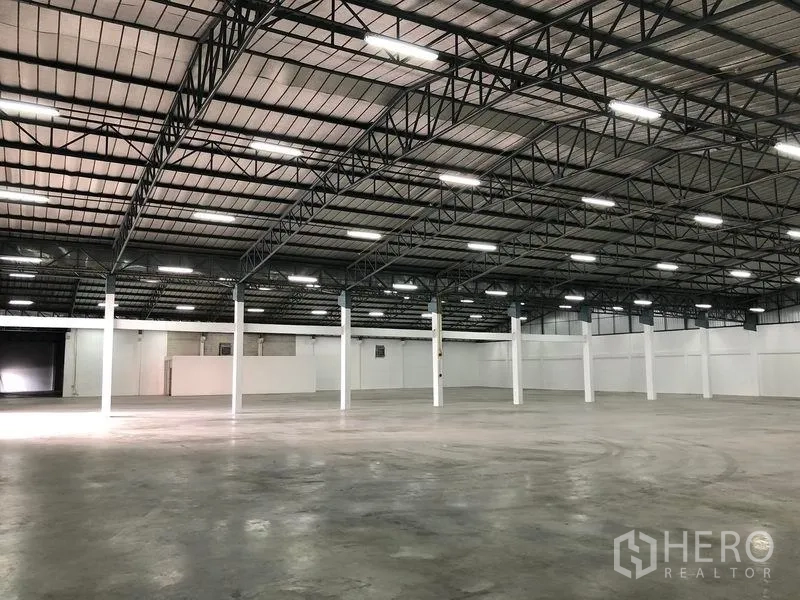 Warehouse for rent in Pak Kret, Nonthaburi - Open interior showing steel truss ceiling, smooth concrete flooring and white perimeter walls.