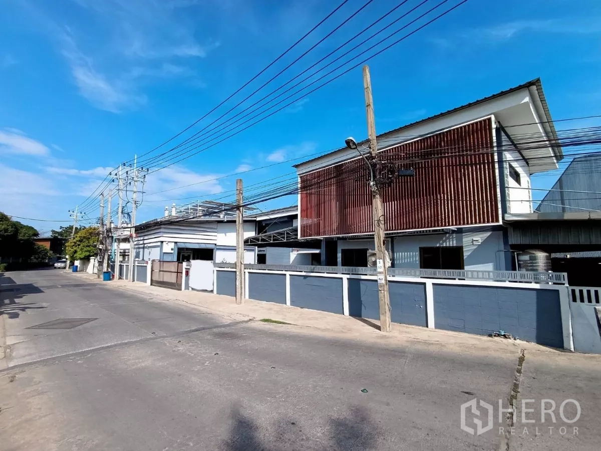 工厂 出租或出售在Bang Khun Thian, Bangkok - 工厂转角立面，长围墙与红色格栅上层立面，在晴空下清晰可见。