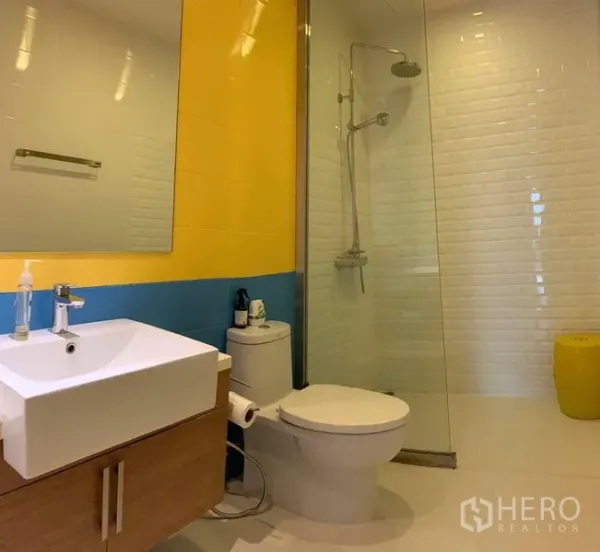 คอนโด ให้เช่าในPhaya Thai, Bangkok - ห้องน้ำโมเดิร์น มีกระจกกั้นอาบน้ำแบบเรนชาวเวอร์ ผนังเหลือง–น้ำเงิน และอ่างล้างหน้า