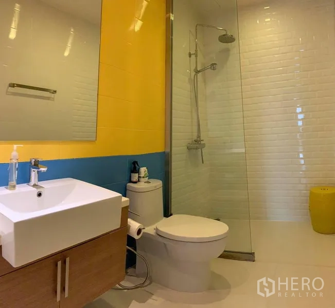 คอนโด ให้เช่าในPhaya Thai, Bangkok - ห้องน้ำโมเดิร์น มีกระจกกั้นอาบน้ำแบบเรนชาวเวอร์ ผนังเหลือง–น้ำเงิน และอ่างล้างหน้า