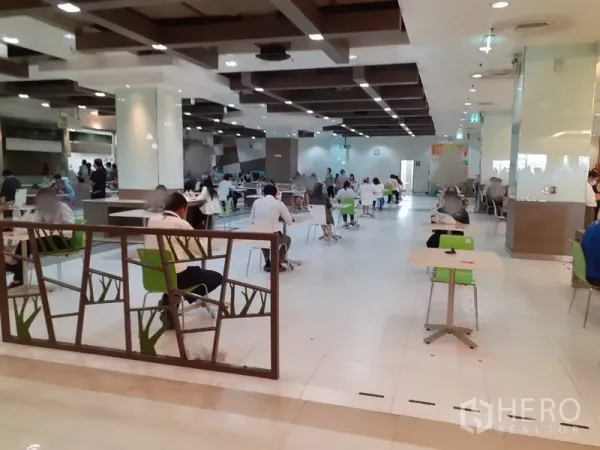 Office Space for rent in Bang Na, Bangkok - Modern building cafeteria with tables, green chairs and wood-accent ceiling.