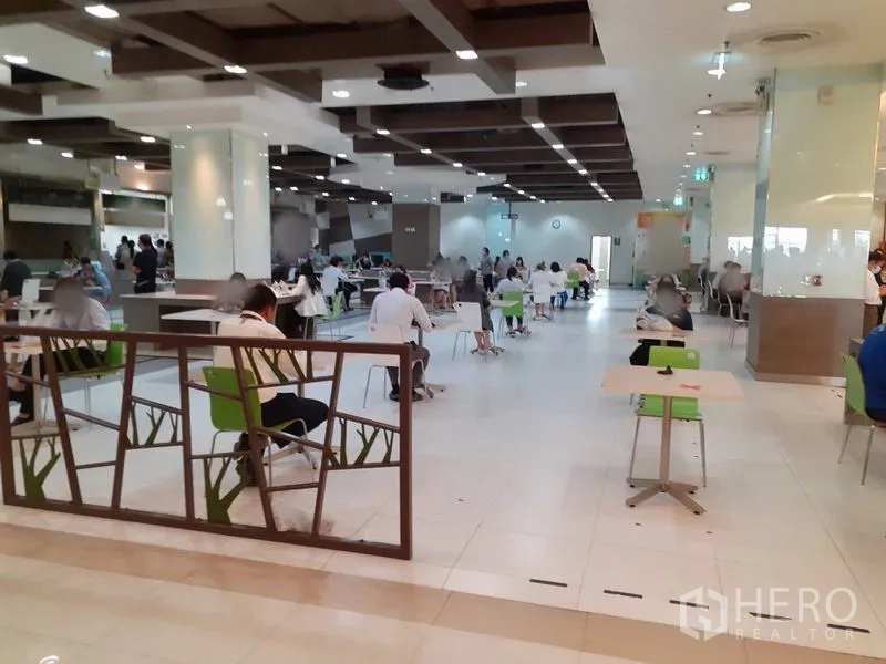 Office Space for rent in Bang Na, Bangkok - Modern building cafeteria with tables, green chairs and wood-accent ceiling.