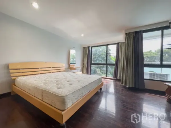 Condominium for sale in Samut Prakan - Bright master bedroom with double bed, wood floors and large windows facing greenery.