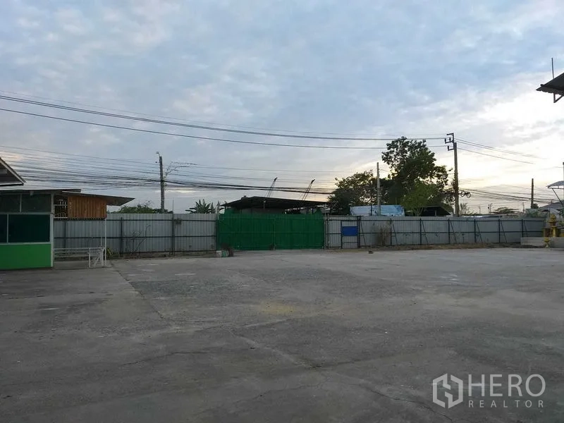 คลังสินค้า ให้เช่าในKhlong Sam Wa, Bangkok - ลานคอนกรีตโล่งพร้อมรั้วรอบและประตูสีเขียว มีสายไฟเหนือศีรษะ